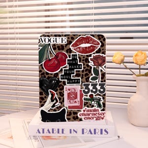Könnte beinhalten: Eine Tablet-Hülle mit Leopardenmuster und verschiedenen Aufklebern, darunter rote Kirschen, Lippen, eine Rose und die Texte "VOGUE", "DO WHAT MAKES YOUR SOUL HAPPY", "333" und "main character energy".