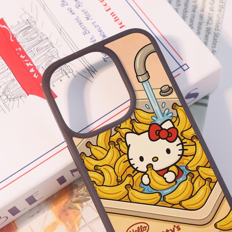 Może przedstawiać: Etui na telefon z motywem Hello Kitty otoczone bananami pod kranem. Projekt zawiera czerwoną kokardę, ż&oacute;łte banany i tekst "Hello Kitty's". Obudowa ma brązową obw&oacute;dkę.