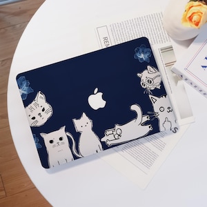 May include: A navy blue laptop case featuring a white Apple logo and playful cartoon cat illustrations. The cats are in various poses, with some wearing glasses and others with expressive gestures. Blue floral accents are also present.