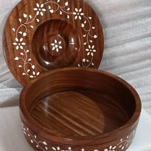 May include: A two-piece wooden serving set with a rich brown finish. The set includes a round bowl and a lid, both adorned with delicate white floral and vine patterns. The bowl is approximately 20 cm in diameter, and the lid is slightly larger.
