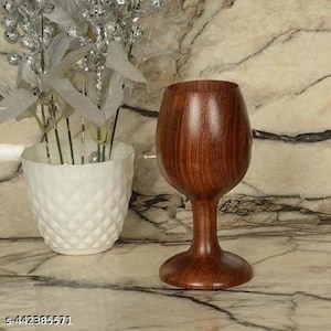 Può includere: Un calice da vino in legno fatto a mano con una finitura marrone scuro. Il calice presenta un gambo classico e una coppa ampia e arrotondata. La venatura del legno è visibile, aggiungendo alla sua estetica naturale. Il calice è esposto su una superficie di marmo.