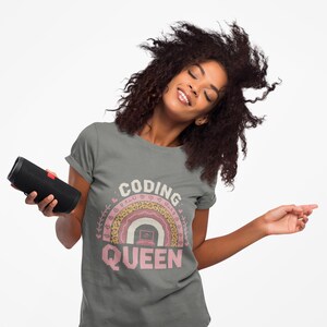 May include: A gray t-shirt with the text "CODING QUEEN" in pink, featuring a rainbow design with a laptop graphic. The shirt is being worn by a person holding a black speaker.