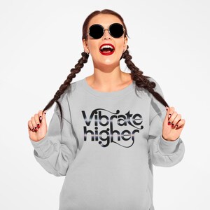 May include: A gray sweatshirt with the text "Vibrate Higher" printed in black with a silver glitter effect.