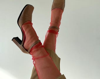 Puede incluir: Un par de zapatos marrones de tacón con calcetines de malla roja. Los zapatos tienen una punta cuadrada y un tacón grueso.