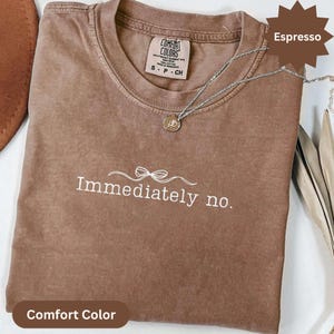 May include: Espresso-colored Comfort Colors t-shirt with the phrase "Immediately no." in white script. A silver necklace with a pendant rests on the shirt. The shirt has a crew neck and a small tag.