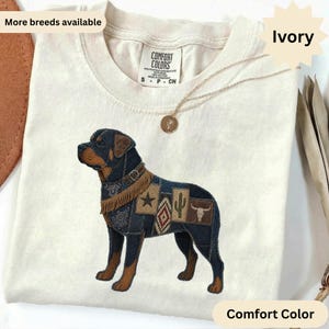 Peut inclure: Un t-shirt ivoire avec un motif de chien Rottweiler composé de divers empiècements en jean et en tissu à motifs. Le design du chien comprend un collier à franges, une étoile, un cactus et un crâne de bœuf. Étiquette Comfort Colors.