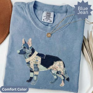 Puede incluir: Una camiseta de color azul vaquero con un gráfico de un pastor alemán en patchwork hecho de varios retazos de tela vaquera y floral. La camiseta tiene cuello redondo, una etiqueta de la marca Comfort Colors y un collar de cadena dorada.