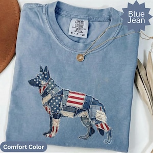 Puede incluir: Camiseta Comfort Colors azul vaquero con un diseño patriótico de perro. El perro está hecho de parches de mezclilla con detalles de la bandera estadounidense. Un collar dorado con un colgante está sobre la camisa.