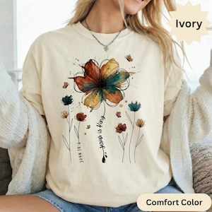 May include: Ivory Comfort Color t-shirt with a large floral design in brown, yellow, and teal watercolour style. The text "Jesus is King" and "John 14:6" are printed on the shirt, along with small flower and butterfly illustrations.