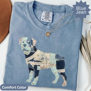 Op de afbeelding: Een blauw spijkerkleurig t-shirt met een Comfort Colors merklabel in de nek. Het shirt is voorzien van een grote applicatie van een hond, samengesteld uit diverse stoffen lapjes, waaronder denim, bloemenprints, groen gingham en kanten details.