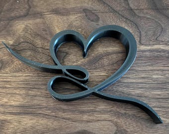 May include: A black, 3D printed heart-shaped design with a stylised swirl inside. The heart is on a wooden surface.