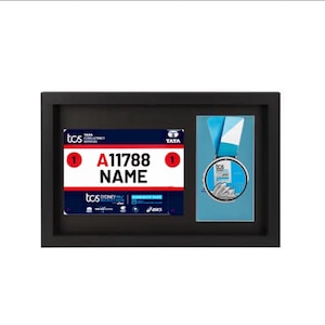 May include: A black framed display with a silver medal and a white and red race bib. The bib has the text "TCS Sydney Marathon" and "A11788 NAME".
