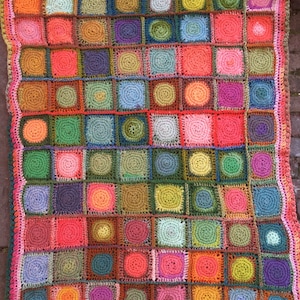 May include: A colorful crocheted blanket with a variety of squares in different colors and patterns. The blanket is made with a variety of yarns in shades of green, red, orange, purple, blue, and brown.