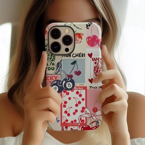 May include: A phone case with a collage design featuring cherries, hearts, and the text "MON CHÉRI". The case has a white background with pink and blue accents. The design includes a cherry with the number 8 and the word "LUCKY".