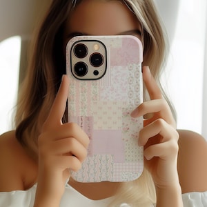 May include: A pink and white patterned phone case with a camera lens cutout. The case has a patchwork design with floral and geometric patterns.