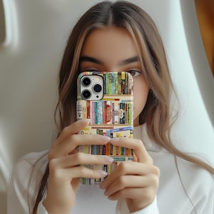 May include: A smartphone case featuring a colorful bookshelf design. The case displays rows of books with various spines, creating a vibrant and literary aesthetic. The case is held in front of a person.