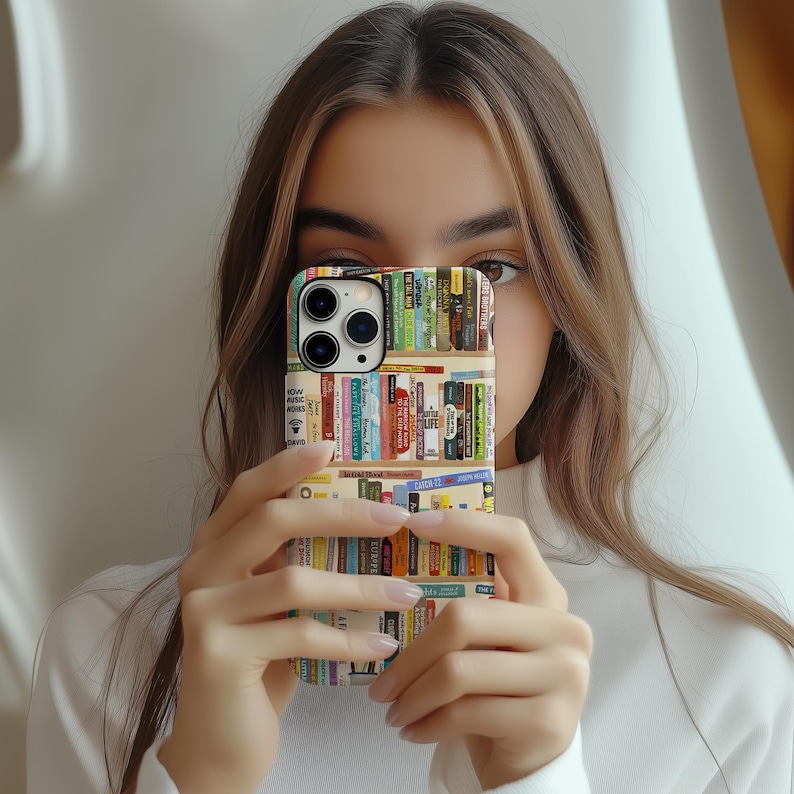 May include: A smartphone case featuring a colorful bookshelf design. The case displays rows of books with various spines, creating a vibrant and literary aesthetic. The case is held in front of a person.