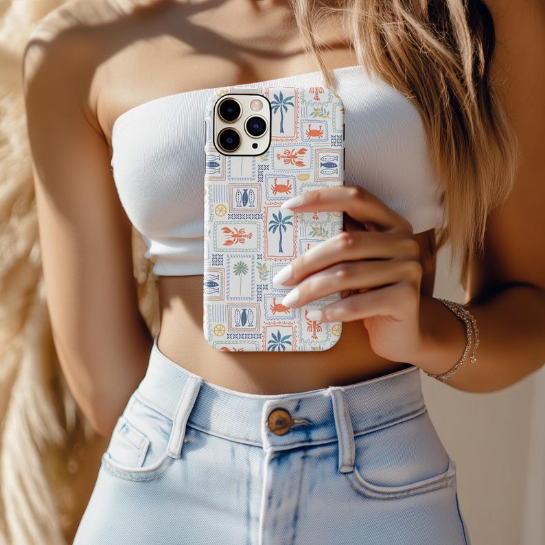 May include: A white iPhone case with a colorful, repeating pattern of stamps featuring palm trees, crabs, fish, and lobsters. The case has a protective design and is held in front of a person.