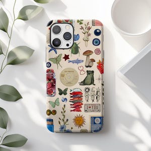 May include: A beige phone case featuring a collage of whimsical illustrations. The design includes strawberries, mushrooms, butterflies, fish, a frog, and a vinyl record. The text "I ♥ YOU" is also visible.