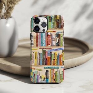 May include: A phone case featuring a colorful bookshelf design. The case displays a variety of book spines with titles like "Catch-22" and "Northern Lights". The case has a glossy finish and is designed to fit a smartphone.