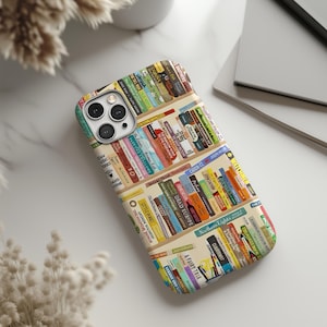 May include: A smartphone case featuring a colorful bookshelf design. The case displays a variety of book spines with titles and authors, creating a literary theme. The case has a beige background and a glossy finish.