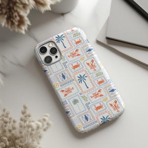 May include: A white phone case featuring a repeating pattern of postage stamp-style designs. The stamps include illustrations of palm trees, crabs, lobsters, fish, and surfboards in blue, orange, and green. The case is on a white marble surface.