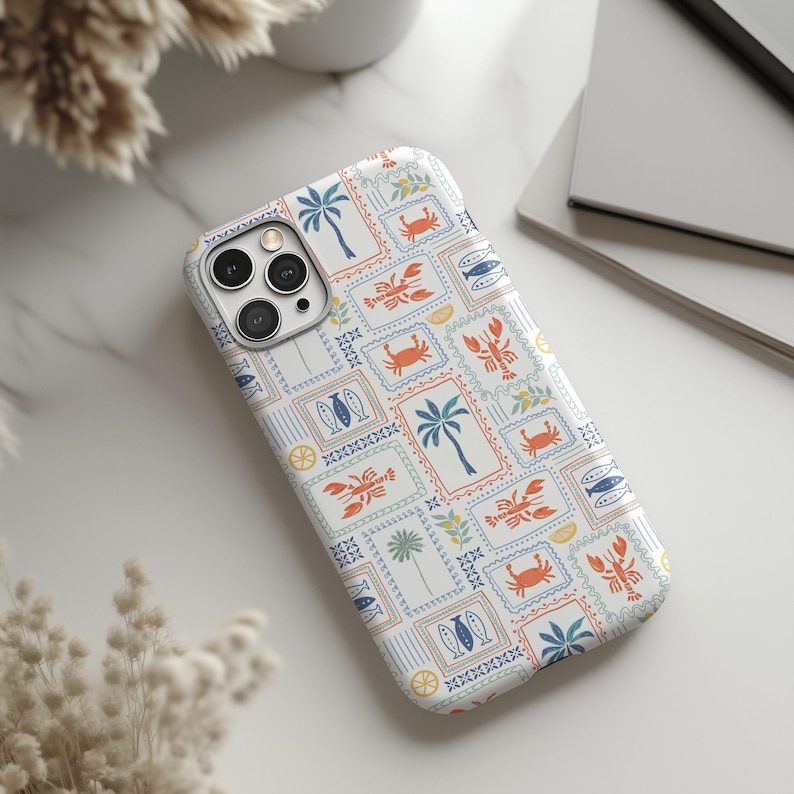 May include: A white phone case featuring a repeating pattern of postage stamp-style designs. The stamps include illustrations of palm trees, crabs, lobsters, fish, and surfboards in blue, orange, and green. The case is on a white marble surface.