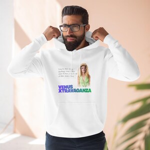 Pode incluir: Moletom branco com o texto "VENUS XTRAVAGANZA" em roxo e verde. O moletom apresenta um retrato de uma mulher em um top verde e o texto "Touch this shirt darling, touch this shirt honey, touch all of this shirt Okay?!"