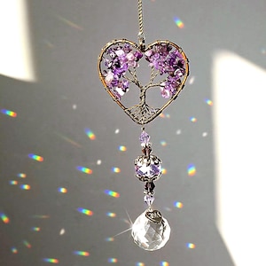 May include: A heart-shaped suncatcher with a wire tree design filled with purple gemstones. The suncatcher hangs from a chain and features a faceted crystal ball at the bottom. The suncatcher is approximately 6 inches long.