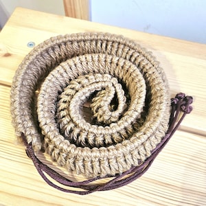Peut inclure: Une corde enroulée en fibre naturelle de couleur brune. La corde est munie d'un cordon brun foncé.