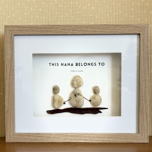 May include: A framed artwork featuring a pebble art design of a mother and two children. The artwork is set against a white background and includes the text "This Nana Belongs To" with the names "Everly & Eliana" underneath.