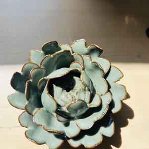 以下が含まれることがあります： 緑と茶色のセラミック製の花の装飾品。 花びらは質感があり、光沢のある仕上がりです。 手作りのアイテムで、インテリアに自然の雰囲気を加えます。