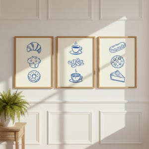Może przedstawiać: Trzy oprawione wydruki artystyczne z jasnobeżowym tłem i niebieskimi rysunkami linii jedzenia i kawy. Lewy wydruk przedstawia rogalik, babeczkę i pączka. Środkowy wydruk przedstawia ziarna kawy i dwie filiżanki kawy. Prawy wydruk przedstawia ekler, ciastko i kawałek ciasta.