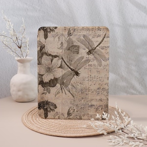 Könnte beinhalten: Ein Buchcover im Vintage-Stil mit einem floralen Design und Libellen. Der Hintergrund zeigt Noten und eine verblasste, strukturierte Optik.