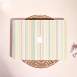 May include: A laptop computer featuring a protective skin with a vertical striped pattern in soft pastel shades of yellow, green, pink, and blue. The center of the laptop lid displays a white Apple logo, contrasting against the light-colored stripes.