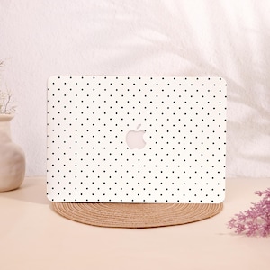 May include: White laptop cover with a black polka dot pattern. The cover features the Apple logo in the center. The laptop is resting on a round, woven placemat. The background is a soft, neutral color.