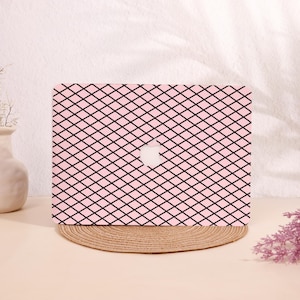 May include: A pink laptop case with a black grid pattern. The case has a cutout for the Apple logo. The case is sitting on a round, woven placemat.