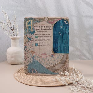 May include: A decorative wooden plaque with a quote from a fairy tale. The plaque has a light beige background with floral and bird designs. The text "dream is a wish your heart makes" is displayed with an illustration of a princess and a castle.