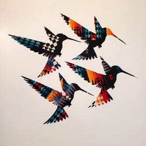 May include: Four hummingbird wall decals featuring geometric patterns in vibrant shades of orange, red, blue, black, and white. Each bird is depicted in a different flight position with sharp, angular wings and long, pointed beaks.