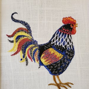 May include: Embroidered kitchen towel featuring a colorful rooster with a red comb, black body, and a yellow, red, and blue tail.