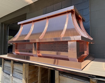 May include: A large, rectangular copper chimney cap featuring a polished, reflective surface, a tiered roof design with vertical textured ribs, and a diamond-patterned mesh screen along the base to provide ventilation and protection for the chimney.