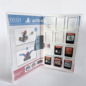 Könnte beinhalten: Ein transparentes Plastik-Etui für Nintendo Switch-Spielkartuschen. Das Etui hat einen weißen Hintergrund mit blauen und roten Akzenten. Das Etui ist geöffnet und zeigt eine Vielzahl von Spielkartuschen, darunter "Crash Bandicoot 4: It's About Time", "Pokémon Schwert", "The Legend of Zelda: Breath of the Wild", "Super Mario Odyssey", "Animal Crossing: New Horizons" und "Kirby und das vergessene Land".