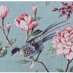 May include: A floral fabric featuring a bird perched on a branch, surrounded by large pink flowers and smaller pink blossoms. The background is a light blue color, creating a soft and elegant design.