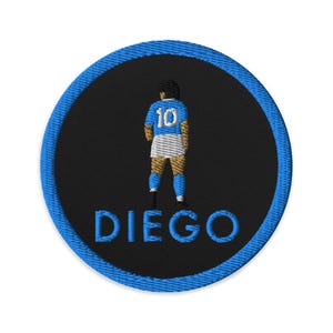 Puede incluir: Un parche bordado azul y negro con un futbolista que lleva una camiseta azul claro con el número 10 en la espalda. El texto "DIEGO" está debajo del jugador.
