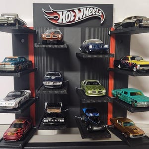 May include: A black and red Hot Wheels display shelf holding various toy cars. The display features the Hot Wheels logo and multiple shelves showcasing a collection of miniature vehicles in different colors and designs.