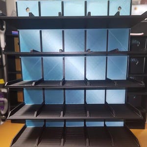 May include: A black plastic shelf unit with five shelves. Each shelf has multiple compartments. The shelves are empty.