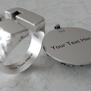 May include: A close-up of a silver ring and pendant. The ring has a unique geometric design with the text "Your Text Here" engraved on the band. The pendant is round with the text "Your Text Here" and the number "925" engraved on it.