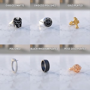 May include: A collection of rings in various styles and finishes. The rings include an oxidized matte skull ring, a polished ring with a crest, a gold-plated ring with a cross, a polished ring with a textured band, a black rhodium plated ring, and a rose gold plated ring.