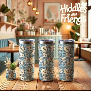 May include: Three stainless steel tumblers with a blue and white checkered pattern and a repeating image of a white bunny sleeping on a cloud with a crescent moon. The tumblers are on a wooden table with a blue and white checkered pattern.