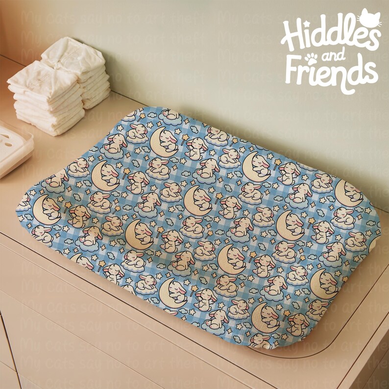 May include: A blue changing pad with a pattern of white bunnies sleeping on clouds with stars and crescent moons. The text "Hiddles and Friends" is in the top right corner of the image.